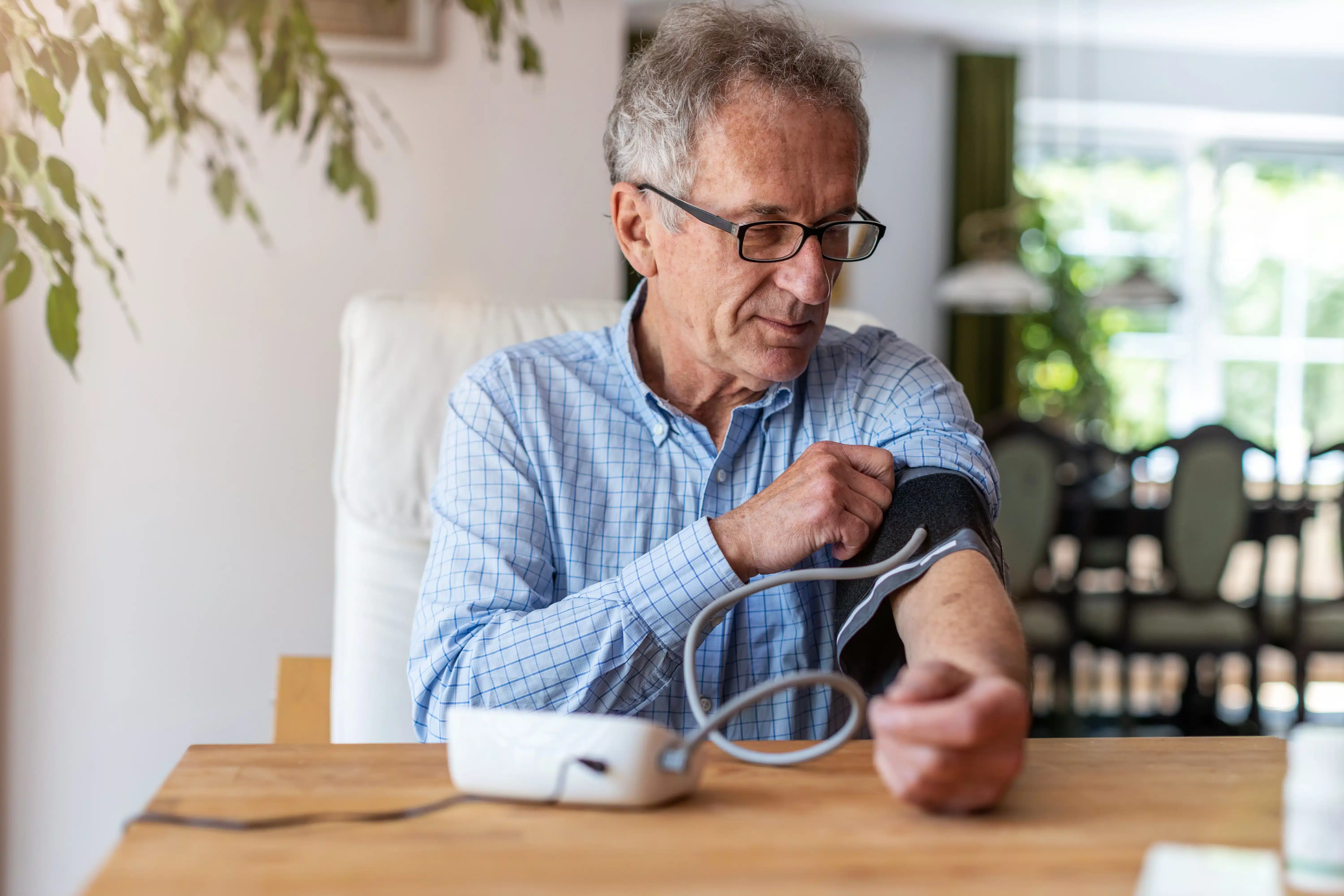 Man sitting at a table at home checking his blood pressure with a monitor.