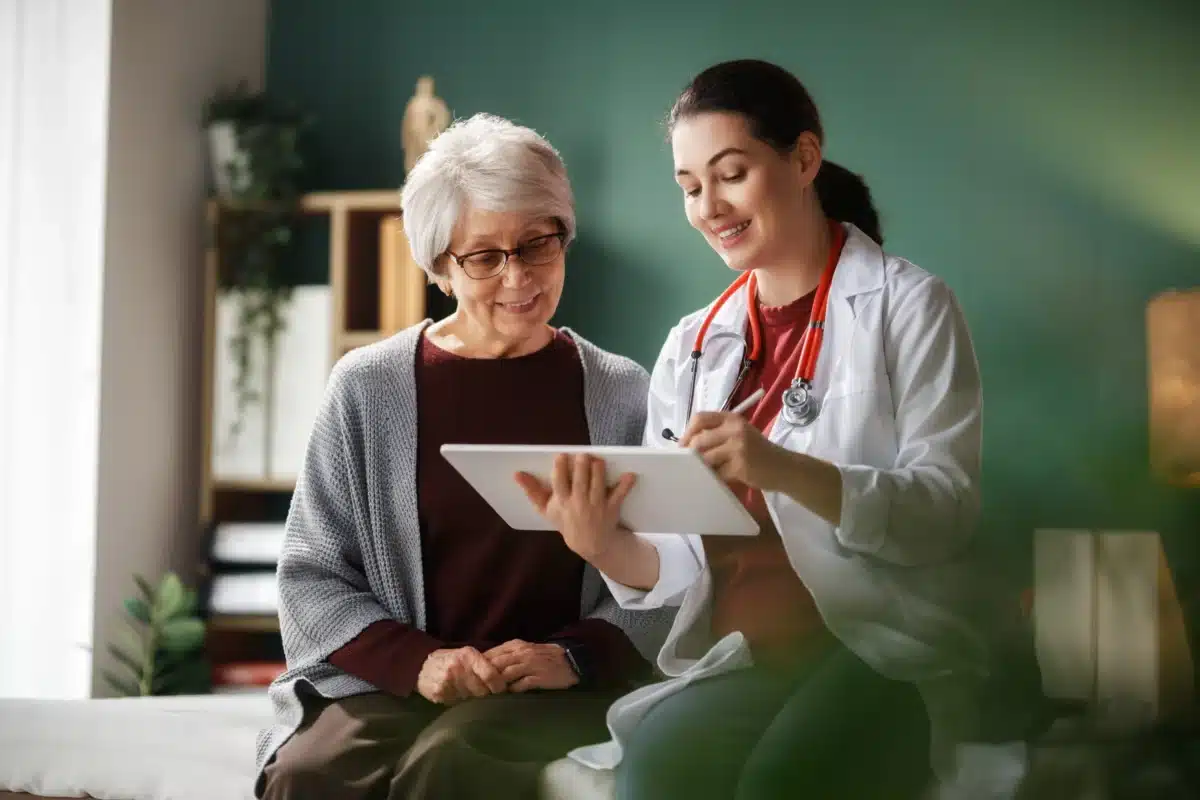 Home visit with a healthcare professional reviewing information on an iPad with an older adult.