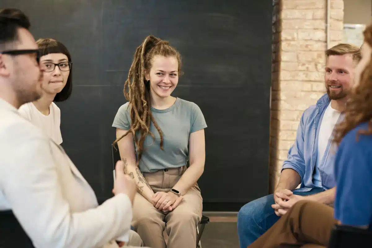 A group of people sitting in a circle during a support group session, smiling and engaging in conversation.